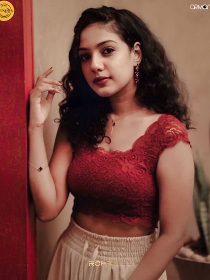 A guest in a red lace top, posing against a red wall.