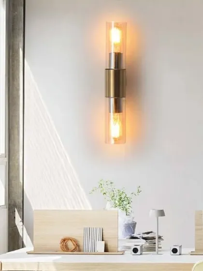 This yellowish rod-shaped wall lamp features a brushed gold finish and two exposed bulbs in amber glass cylinders. The warm light and sleek design make it a perfect accent for a modern office or hallway.