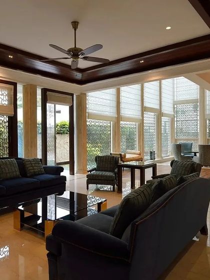 A formal living room that exudes classic elegance with its high-gloss floors, dark wood ceiling trim, and custom jaali screens. The deep blue sofas provide a rich contrast, creating a sophisticated space for hosting guests.