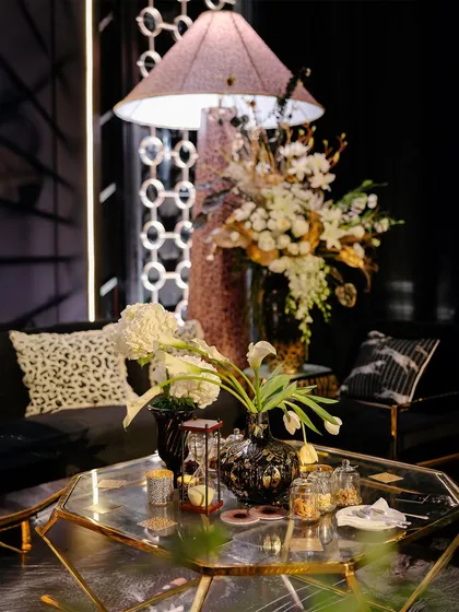 A close-up of the lounge coffee table. Here you can see the mix of textures, from the leopard print cushion and black velvet sofa to the geometric gold-and-glass table. The large floral arrangement adds a touch of natural elegance.