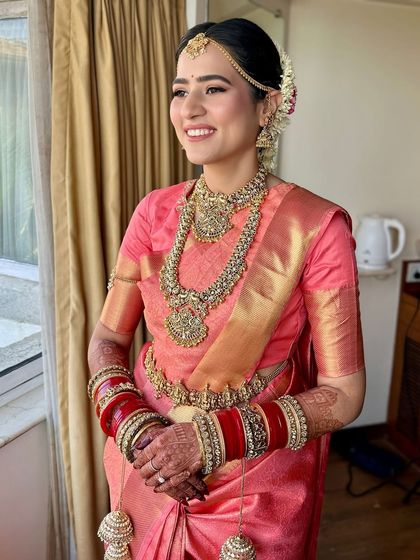 A happy moment captured. The bride's smile is the centerpiece, enhanced by a soft glam look that includes a flawless base, subtly defined eyes, and a natural lip tint, perfect for a South Indian ceremony.