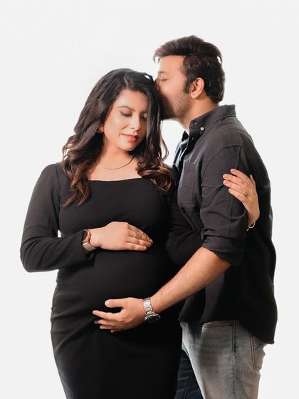 A sweet and tender moment captured in the studio, with the partner gently kissing the mom-to-be's forehead. This pose highlights the protective and loving bond between them.