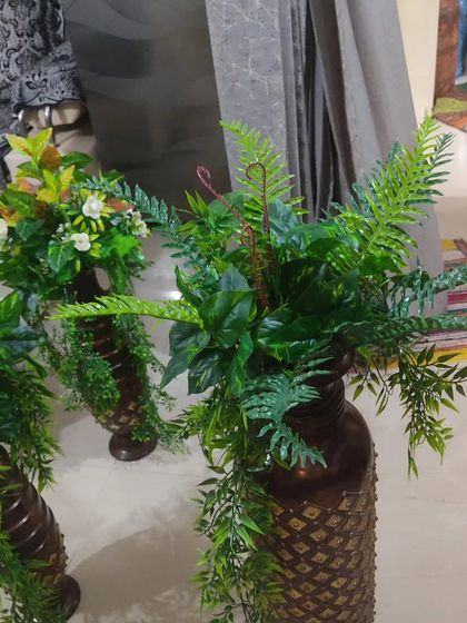 This is a large vase arrangement with a mix of artificial ferns and other green foliage. These are suitable for placing on the floor in corners or next to furniture to add a touch of greenery.