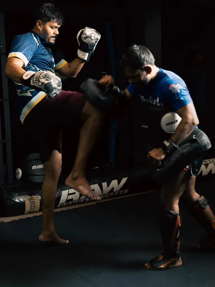 Two fighters spar in a dimly lit setting, highlighting the intensity and focus required during a match. One lands a solid body kick on the pads.