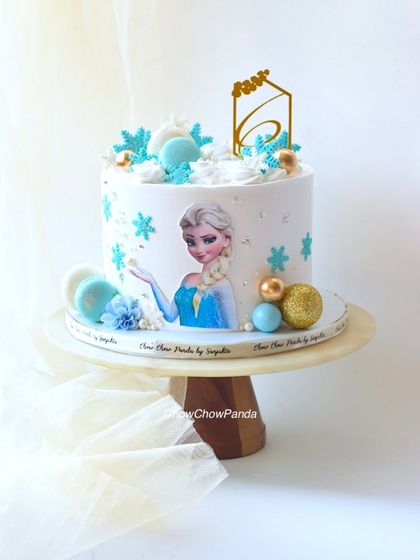 A clear, bright shot of the Elsa theme cake, showing the details of the snowflake decorations and gold topper.