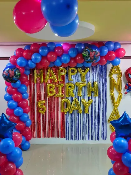 A simple Spiderman theme decoration for a home party. A red and blue balloon arch frames a tinsel curtain with 'Happy Birthday' foil letters.