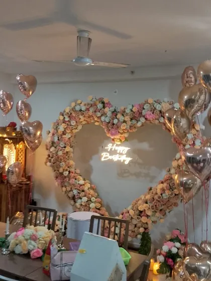 For romantic celebrations, we create breathtaking backdrops like this heart-shaped arch. It's meticulously crafted with artificial roses and florals, accented with a 'Happy Birthday' neon sign and rose gold heart-shaped foil balloons for a truly magical atmosphere.