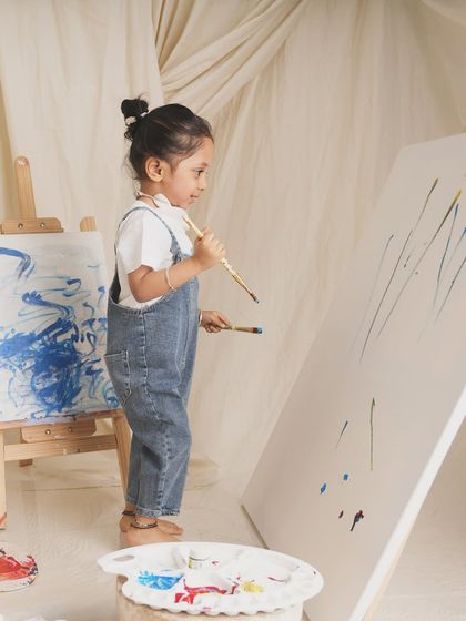 A budding artist stands thoughtfully before her canvas, paintbrush in hand. A beautiful, candid moment of creativity.