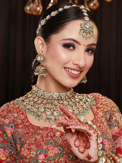 A close-up of a bride's happy face, with her mehandi-adorned hand gently touching her chin, adding to her charm.