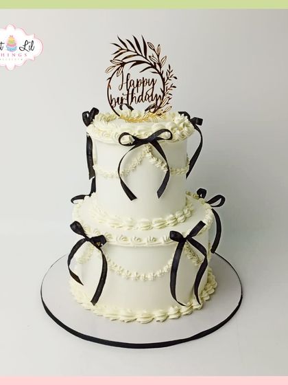 A timeless and elegant two-tiered cake decorated with delicate piping and black ribbons, perfect for a sophisticated birthday.