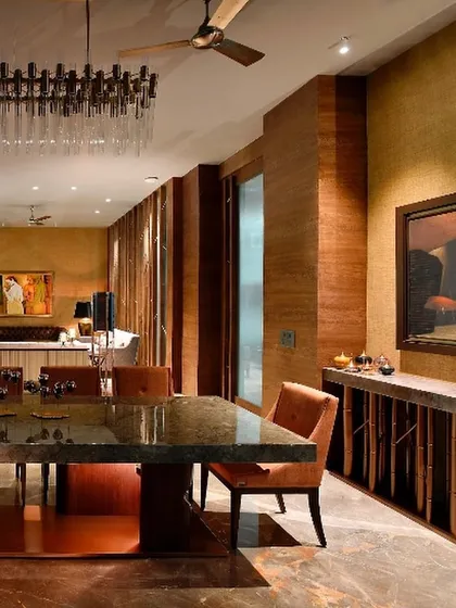 The dining area of a Gurgaon home, where rich textures of wood and stone create a warm and inviting atmosphere. A modern chandelier adds a touch of glamour, while the large windows keep the space connected to the outdoors.