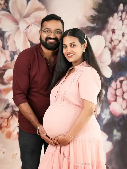 A lovely couple portrait against a soft floral backdrop. The mom-to-be's pink dress and the gentle way they hold the baby bump create a sweet and romantic photo.