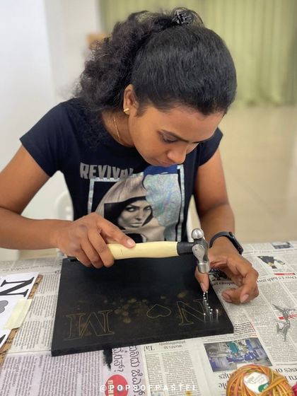 A participant carefully hammers nails for her string art project, showing the focus required for this satisfying craft.
