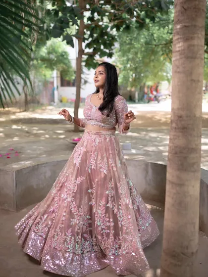 A model twirling in a beautiful pink lehenga, showing the flow and elegance of the outfit, complemented by subtle makeup.