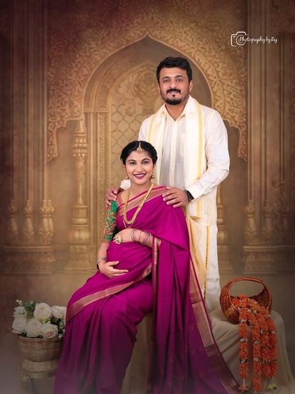 A regal studio portrait of a couple in traditional attire, with the mother-to-be seated and adorned with beautiful jewelry.