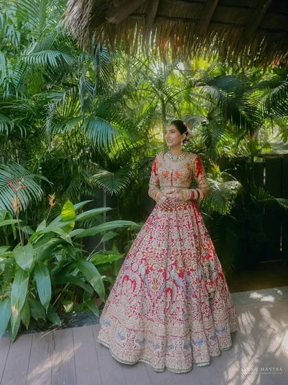 A bride amidst lush greenery. I chose this location for a portrait because the vibrant tropical plants beautifully complemented the intricate floral embroidery on her Rimple and Harpreet lehenga.