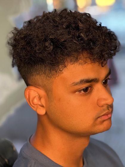 A side profile of a curly hair cut with a fade. The blend is clean and the curls on top are well-defined.