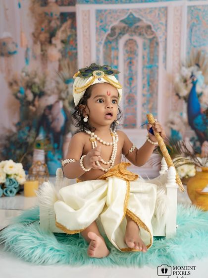 A regal pose for a little deity. This baby boy, dressed as Krishna and holding his flute, looks so majestic in his ornate setting.