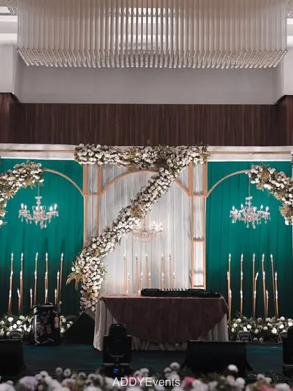 This stage combines emerald green drapery with white floral arrangements and elegant chandeliers. The design is perfect for a formal engagement or a sophisticated corporate event, showcasing a blend of classic and modern aesthetics.