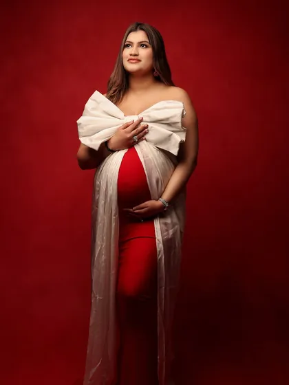 A stunning frontal view of the mother-to-be, wrapped like a precious gift in a red gown and a large white bow. This portrait is a beautiful way to celebrate a pregnancy during the festive season.
