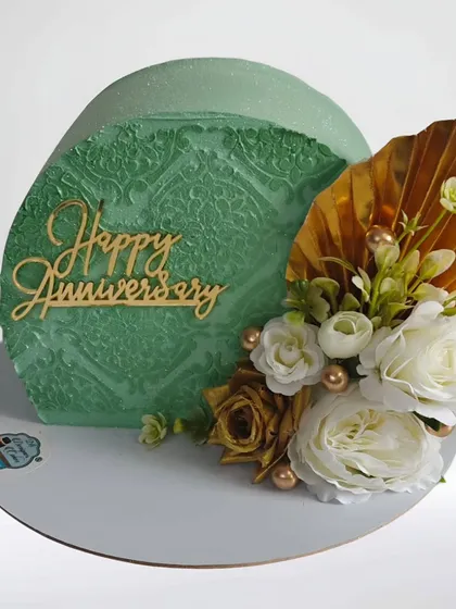 A modern "top forward" anniversary cake with a beautiful sage green stencil pattern. The arrangement of white and gold flowers adds an elegant and artistic flair.