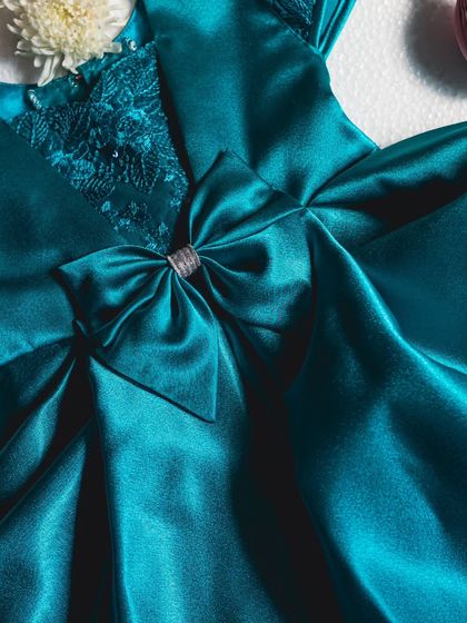 A close-up of this midnight blue satin gown. You can see the intricate sequined lace on the V-neckline and the perfectly centered bow with a silver ribbon detail.