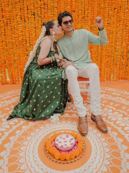 A cute moment between the couple during their Haldi. The bride gives the groom a kiss on the cheek against the vibrant marigold backdrop.