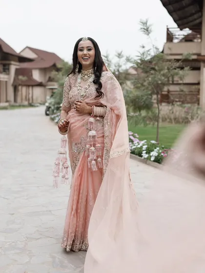 A joyful, candid shot of the bride in a beautiful pink saree, walking with a flowing veil. Her bright smile captures the excitement of her wedding day.