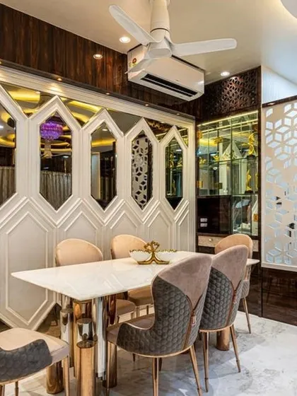 A grand dining area featuring a marble-top table and chairs with quilted upholstery. The wall is adorned with hexagonal mirrors and white paneling, creating a bright and luxurious space for family meals. The design is complemented by a custom bar unit.
