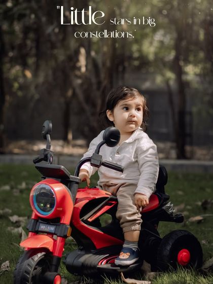 Little stars in big constellations. A toddler sits on his red toy motorcycle, looking off into the distance.