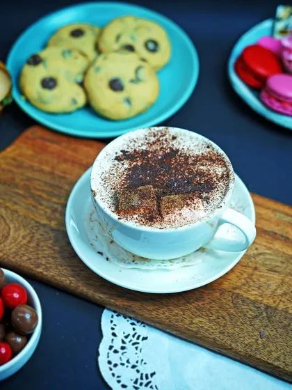 A wider shot of a hot chocolate surrounded by cookies, macarons, and other treats. This composition tells a story of a cozy, indulgent break, great for lifestyle-focused food content.