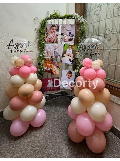 A personalized photo display for Ayzal's first birthday, framed by pink balloon columns and custom bubble balloons.