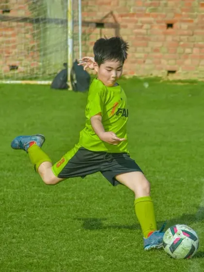 A young player strikes the ball with force, aiming for the goal in a display of developing skill and confidence.