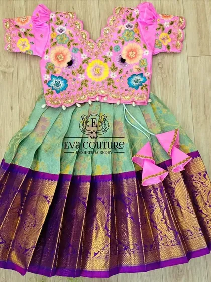 The beauty is in the details. This vibrant lehenga set features a pink blouse with intricate, multi-colored floral threadwork, paired with a light green skirt and a rich purple Kanchi silk border.