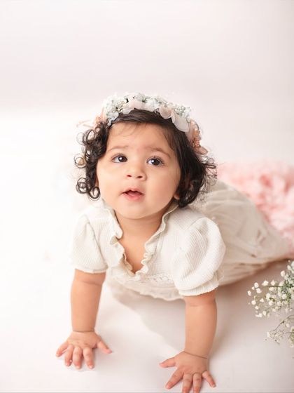 A beautiful crawling shot of an eleven-month-old baby, looking up with her big, curious eyes. The all-white background keeps the focus entirely on her.