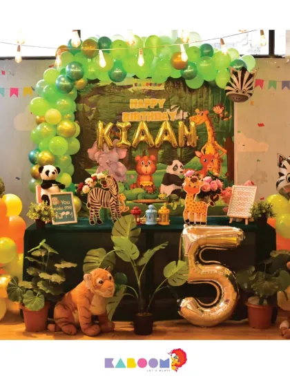 Another view of a fun jungle theme, featuring a vibrant green balloon arch, friendly animal characters, and a large number five balloon for a wild fifth birthday party.