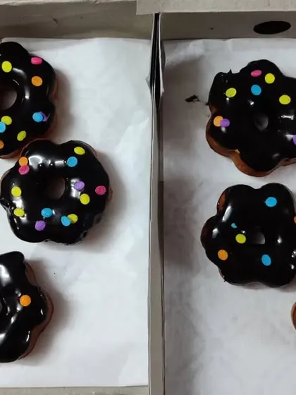 I also make donuts in fun shapes, like these flower-shaped ones. This picture shows both the flower and classic round shapes, all with a dark chocolate glaze and multi-colored sprinkles.