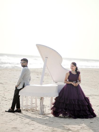 A creative and artistic pre-wedding shoot on the beach with a white piano. The deep purple ruffled gown provides a beautiful, dramatic contrast.