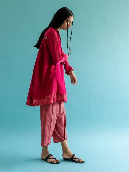 A full-length side profile for Swatti Kapoor. The simple composition against a solid blue wall showcases the silhouette and layering of the contemporary ethnic outfit.
