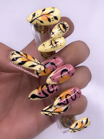 A set of hand-painted press-on nails with a bohemian vibe, featuring sun, moon, snake, and leaf motifs.