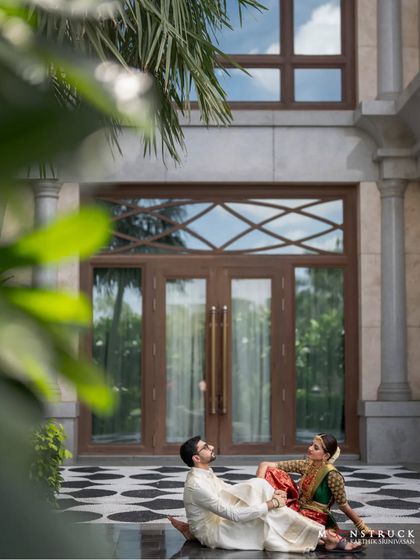 A quiet moment for the couple amidst the wedding festivities. This wide shot showcases their beautiful traditional outfits against the stunning architecture of the venue, the Leela Palace in Chennai.