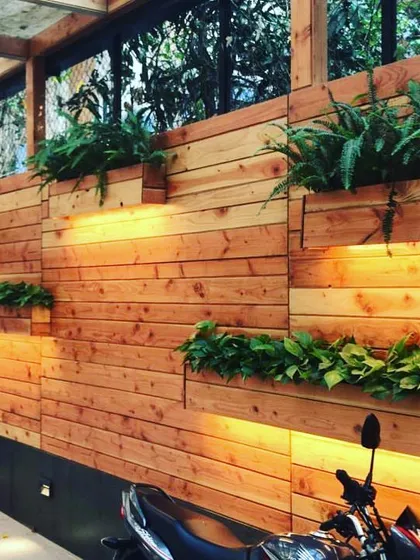 Even a functional space like a driveway can be beautiful. For this Juhu bungalow, we designed and installed a custom wooden wall with integrated planters, using warm lighting to highlight the ferns and money plants.