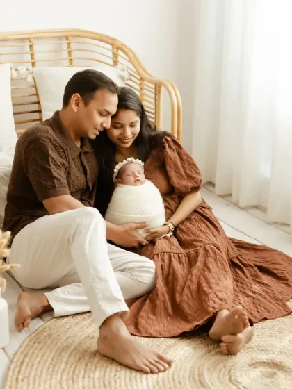 A candid moment during a newborn session. The parents share a smile as they look at their baby, creating a natural and loving family photo.