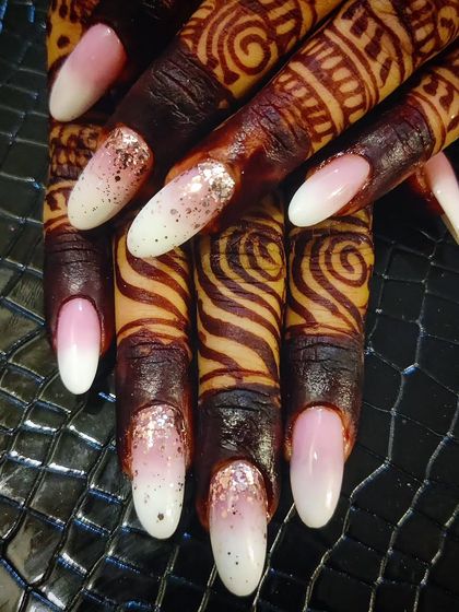 This is a baby boomer or sculpting technique, perfect for a subtle yet stunning bridal look. The seamless gradient from soft pink to white on almond nails is enhanced with a delicate sprinkle of rose gold glitter on the accent nails.