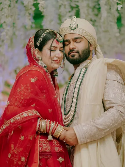 An intimate portrait of a North Indian couple, holding each other close. The rich red of the bride's lehenga and the groom's elegant sherwani create a timeless image of love and commitment.