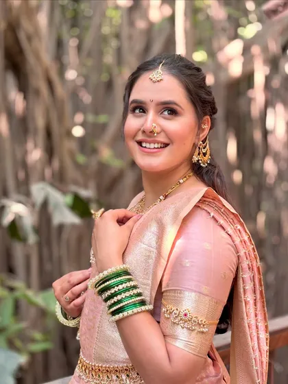 A candid, happy moment captured. Her radiant smile complements the soft pink makeup, traditional green bangles, and gold jewelry, showcasing the complete, joyful look of a Maharashtrian bride.