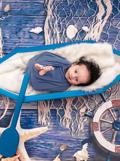 Ahoy, little sailor! This newborn is ready for an adventure in our nautical-themed setup, complete with a boat, fishing net, and starfish for a charming sea-faring portrait.