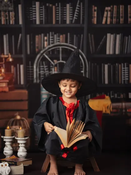 A young wizard smiles as he reads a book of spells. This photo highlights the warm, enchanting atmosphere we create with careful lighting and detailed props for our Harry Potter sessions.