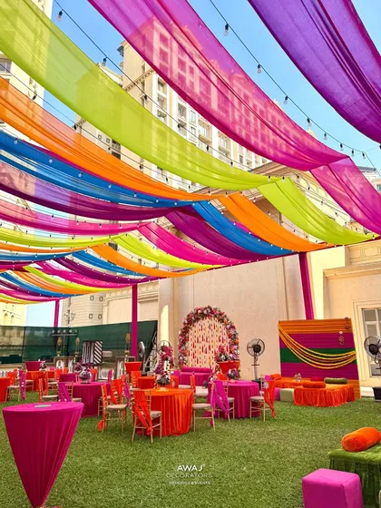 A wide view of an outdoor Mehendi setup, with a rainbow of drapes creating a festive tent over the lawn.