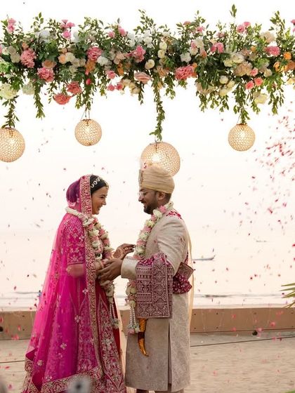 A wide shot of the beachside wedding ceremony, showing the stunning floral arch against the ocean backdrop.